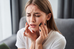 Toothache. Girl suffering from tooth pain and touching cheek while sitting on couch at home. Dental problem concept. Stock photo